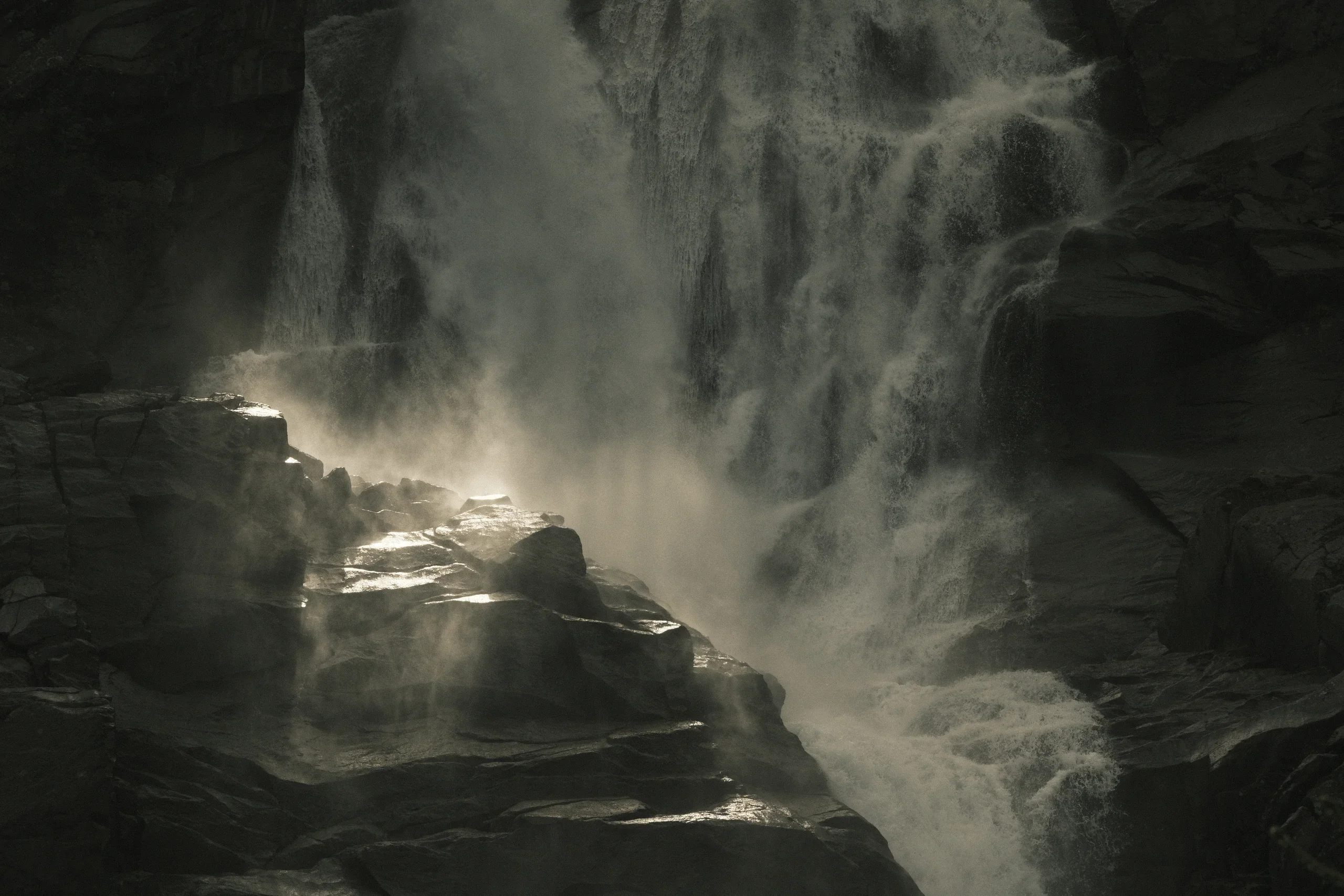 A waterfall breaking through a dark green forest in bright mist